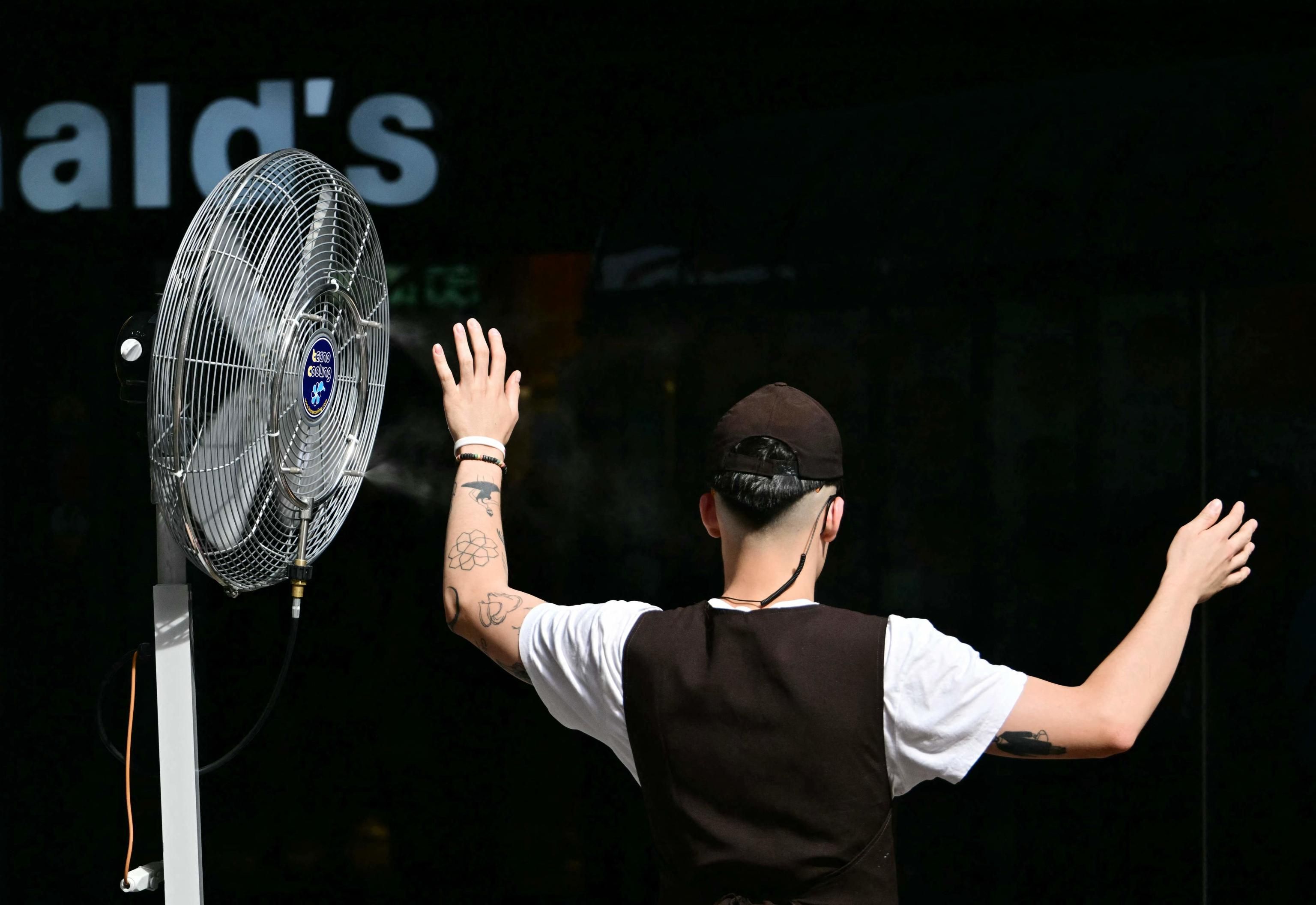 Un dipendente davanti a un ventilatore nebulizzatore si rinfresca sulla terrazza di una gelateria vicino a Piazza del Duomo a Milano. (Foto di STEFANO RELLANDINI / AFP)