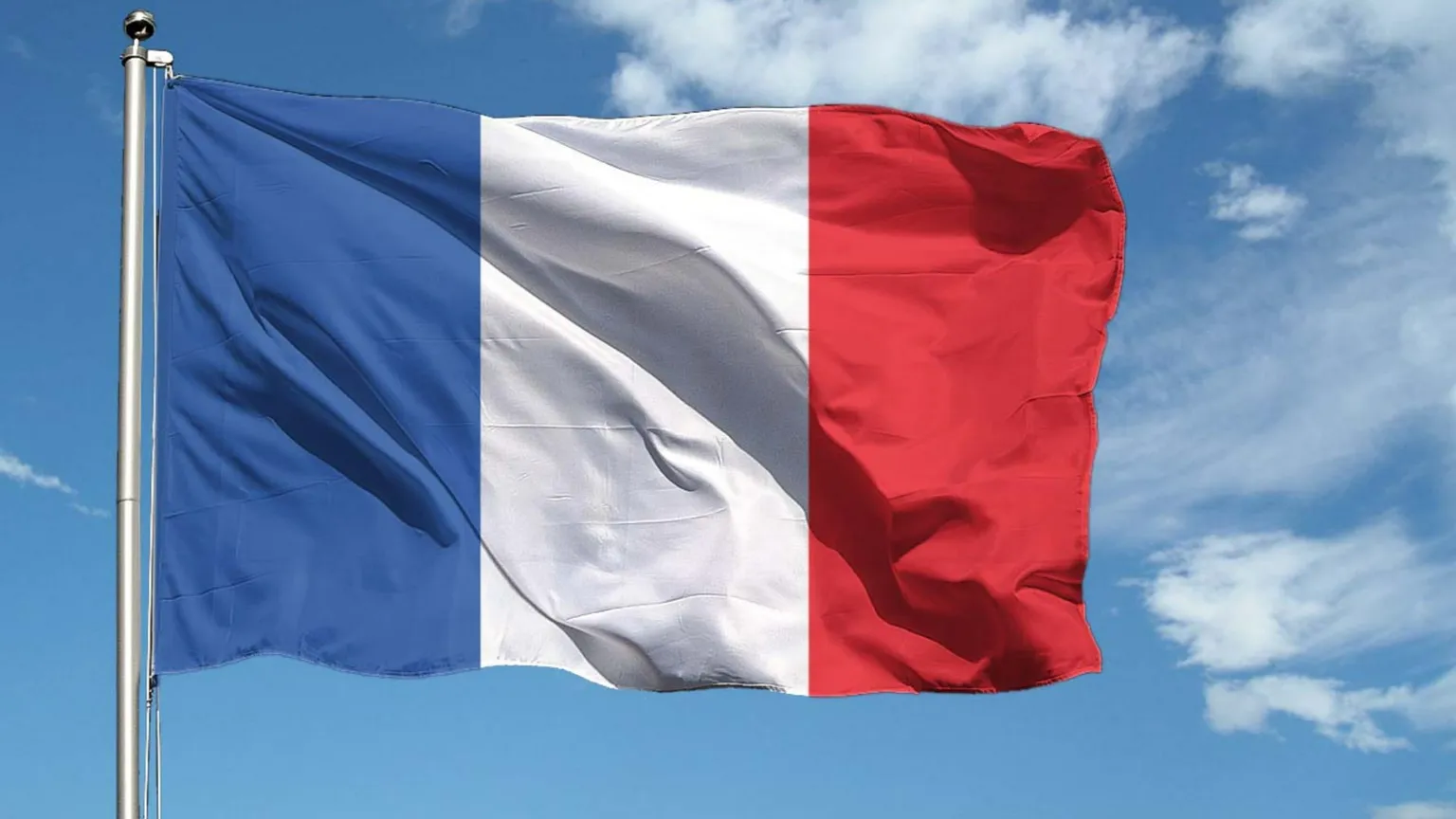 Bandiera francese a tre bande verticali blu, bianca e rossa, fissata a un pennone metallico. Sventola al vento contro un cielo azzurro con qualche nuvola.