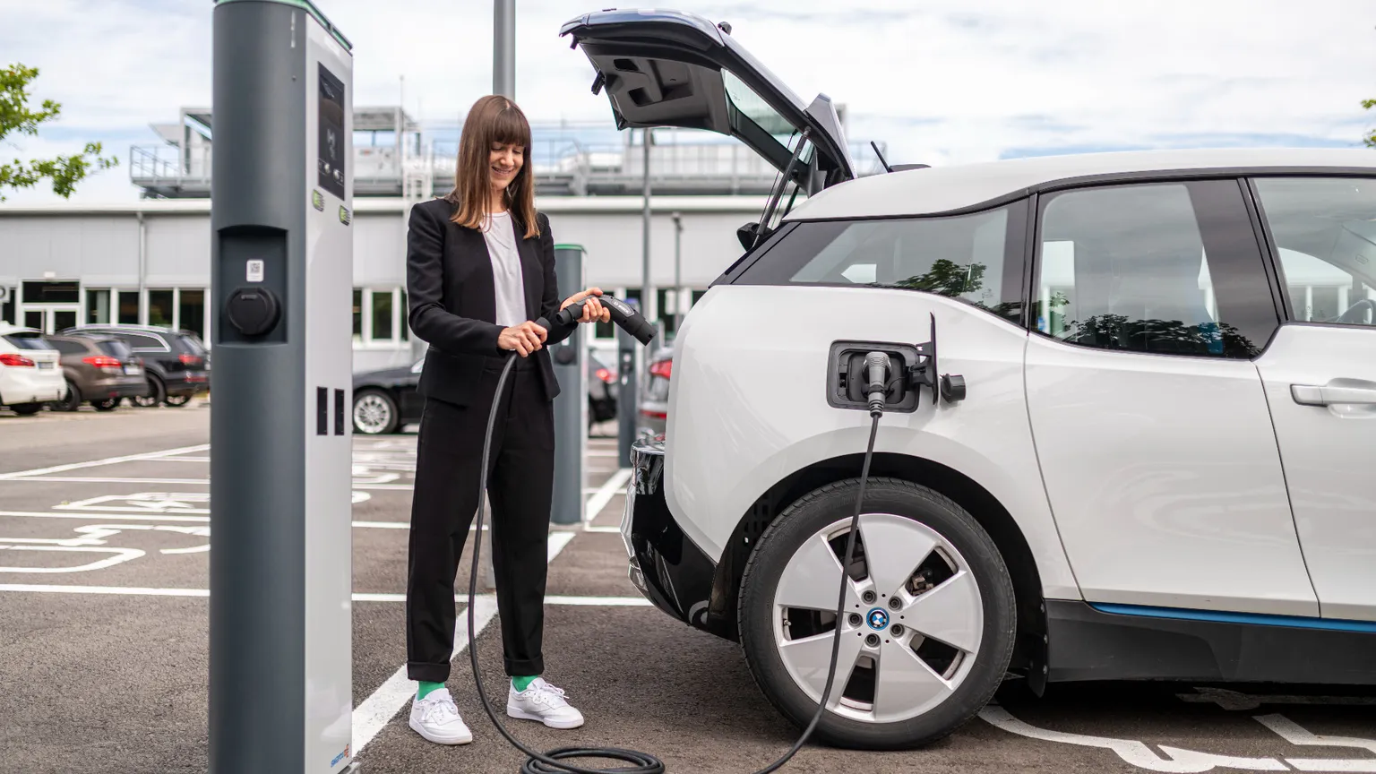 Una ragazza ricarica la propria auto elettrica da una colonnina pubblica