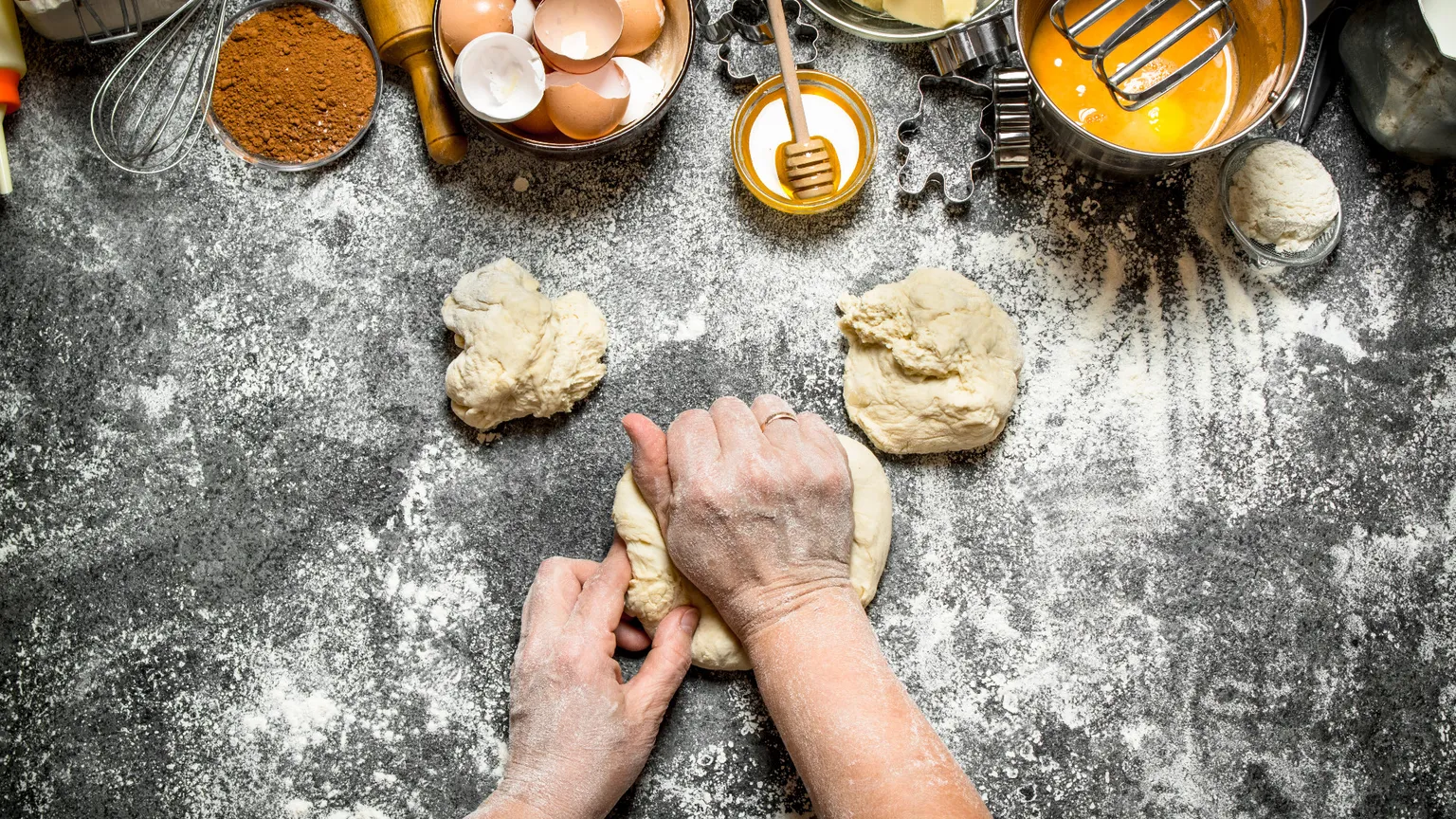 Mani che impastano su un tavolo con farina, uova