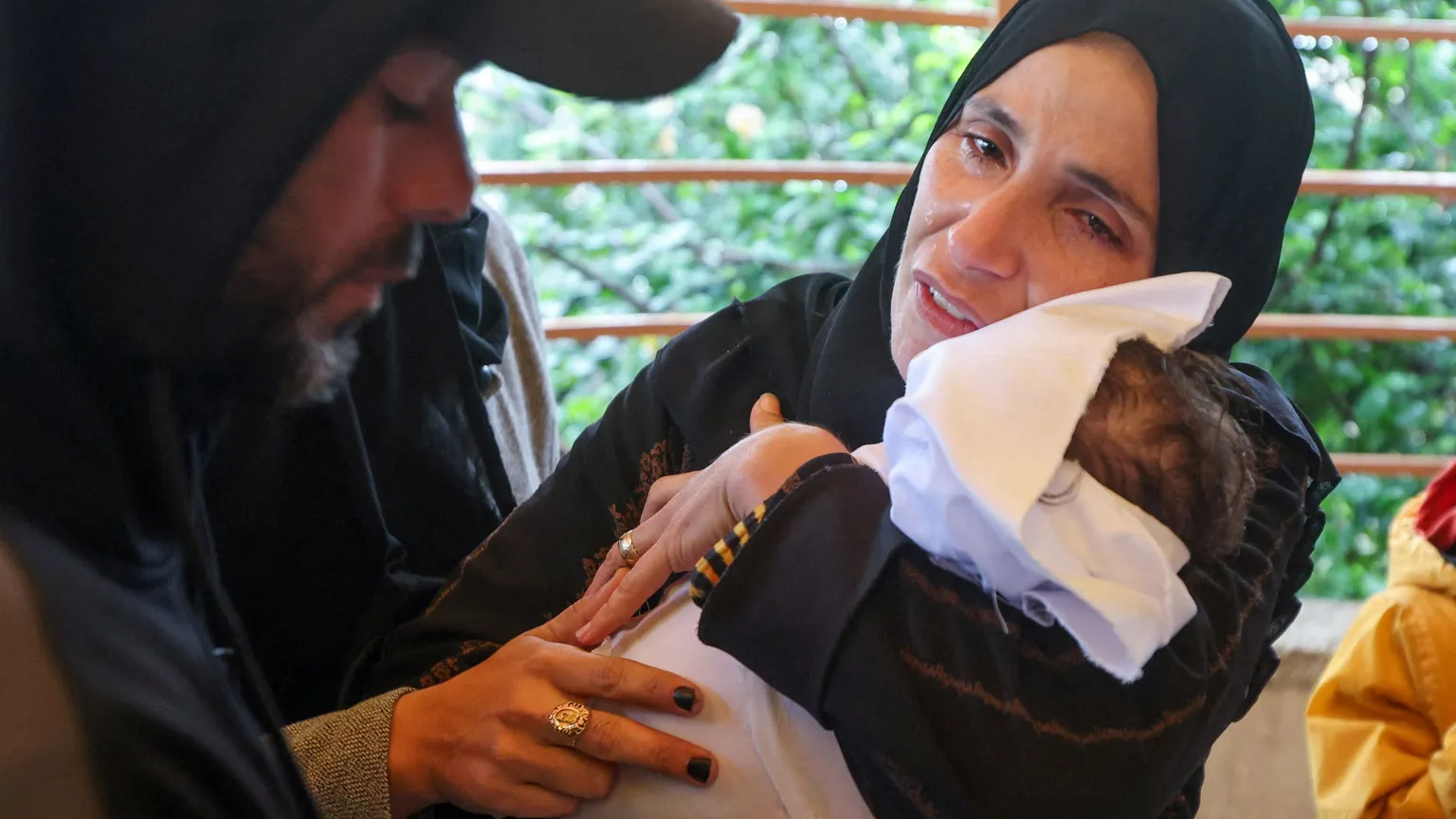 Una donna vestita di nero, con la testa velata e il volto rigato di lacrime, tiene fra le braccia un corpicino avvolto in un sudario bianco