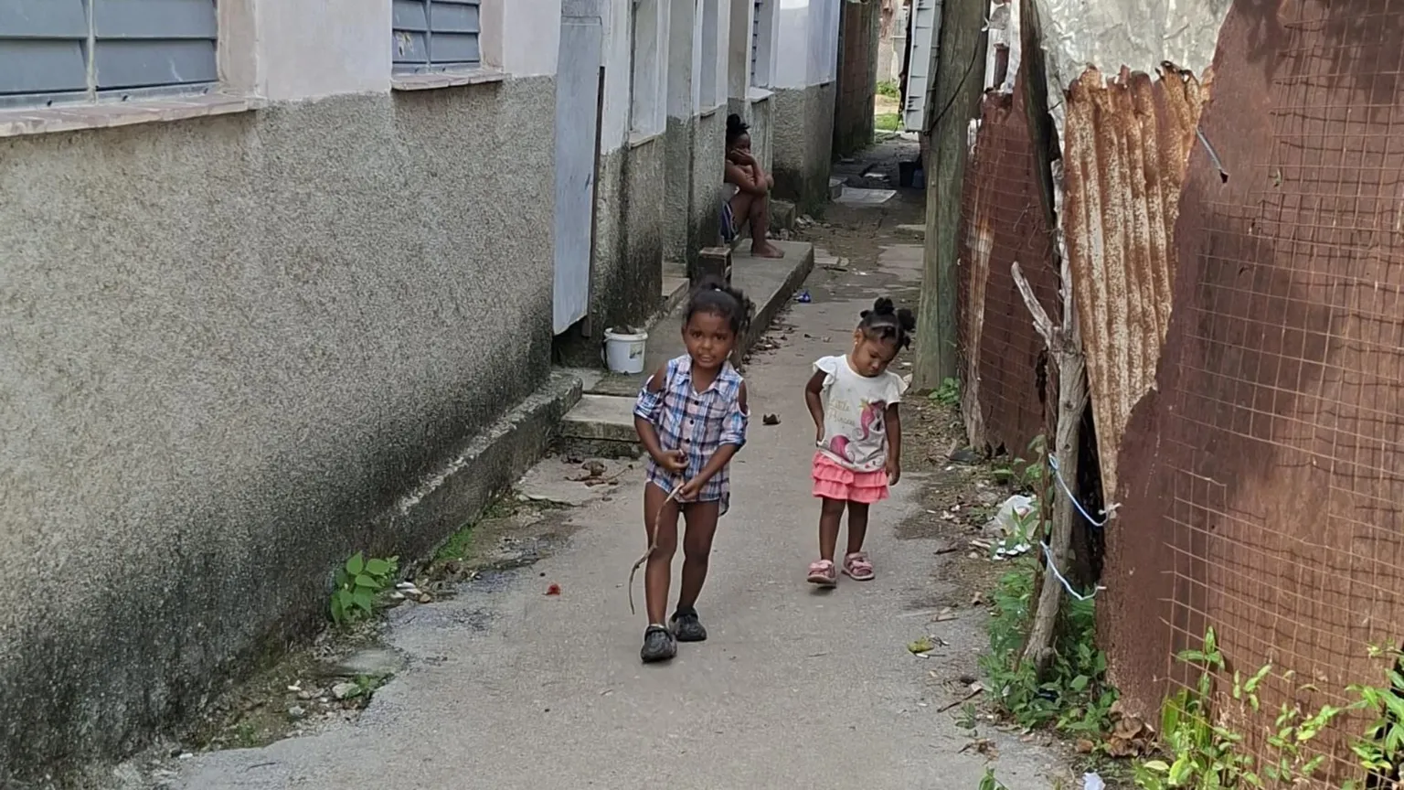 Due bambini cammino in un viottolo sterrato di una baraccopoli dell'Avana su cui si affacciano casupole di compensato e lamiera