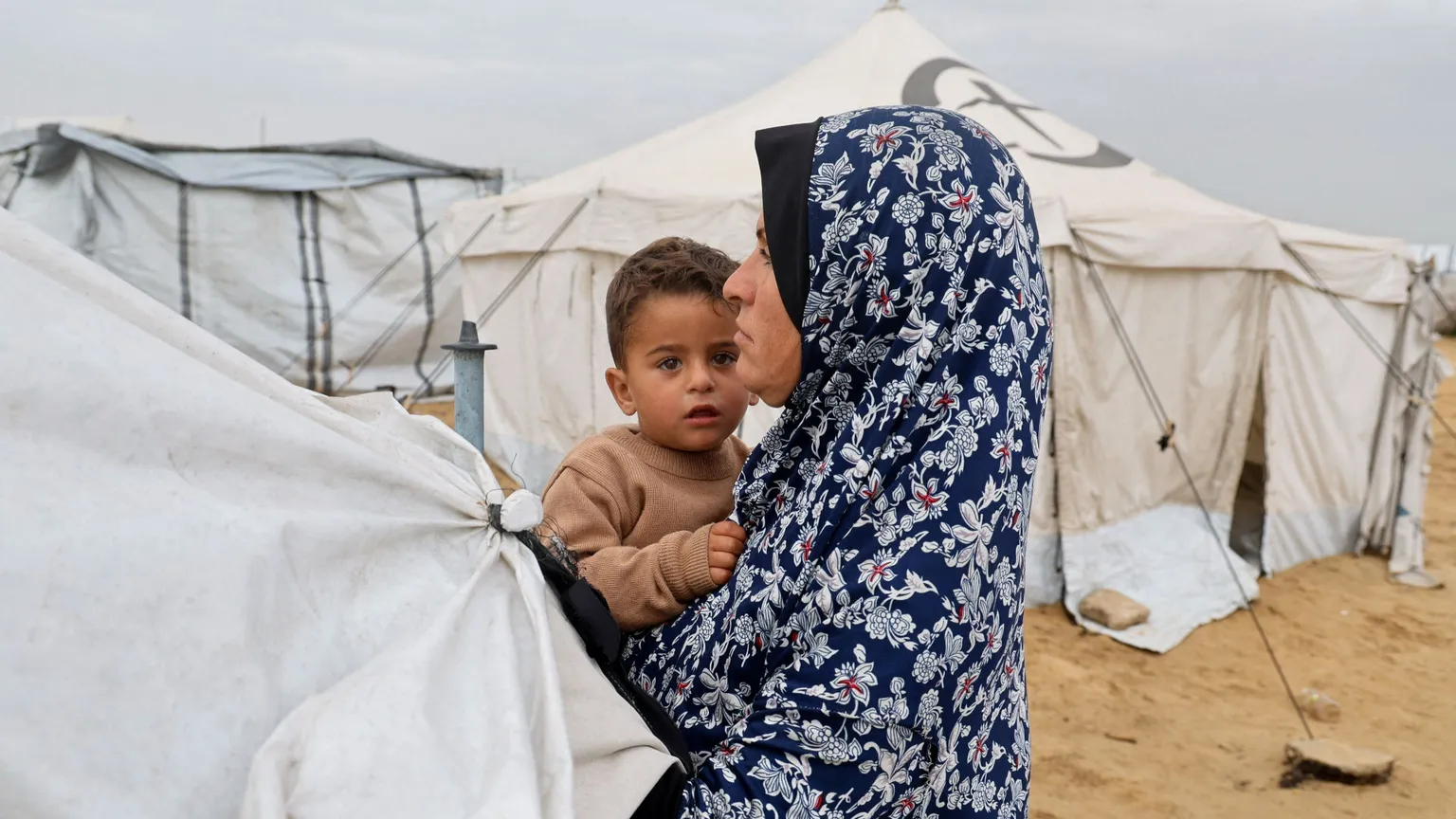 Una donna con in braccia il figlio in una tendopoli per sfollati a Khan Younis, nel sud della Striscia di Gaza