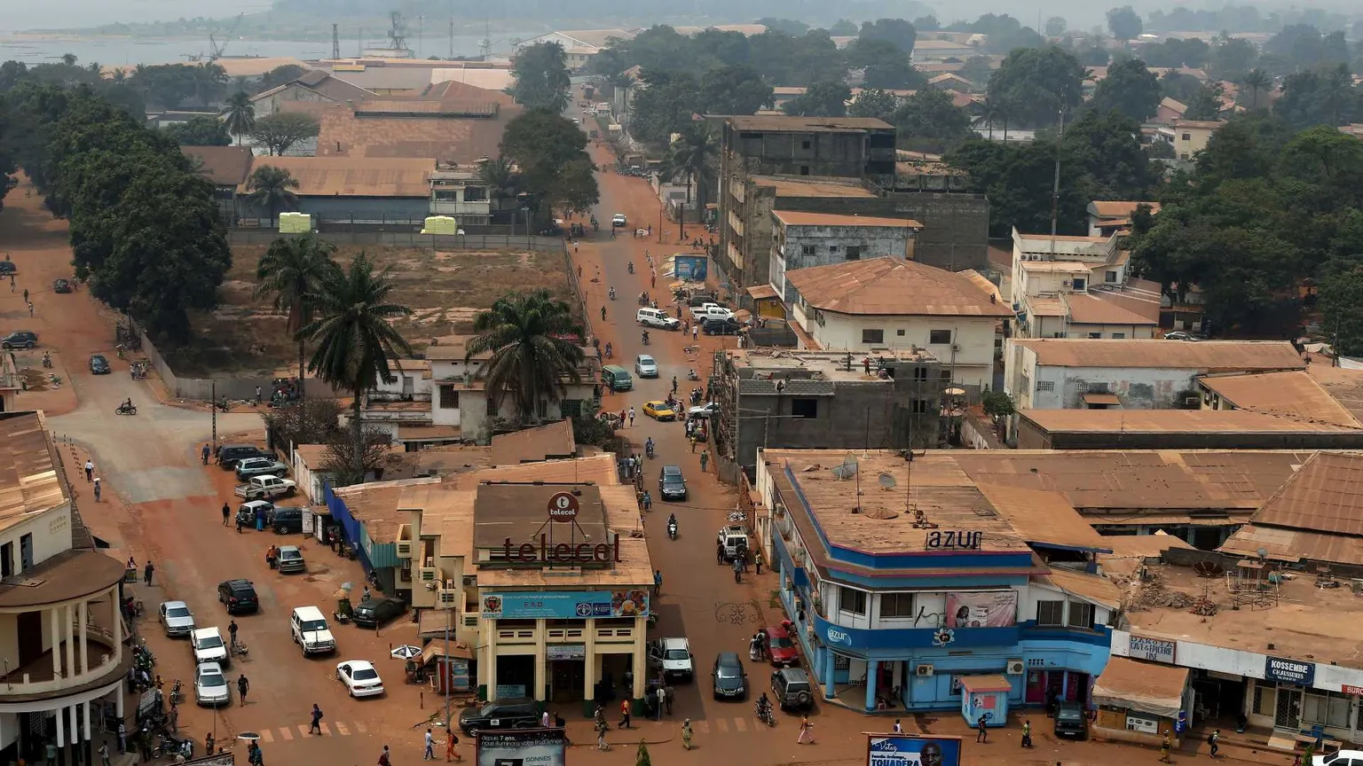 Una strada in terra battuta attraversa la capitale della Repubblica Centrafricana, Bangui. Gli edifici appaiono come fatiscenti. Il colore dominante è l'arancione.