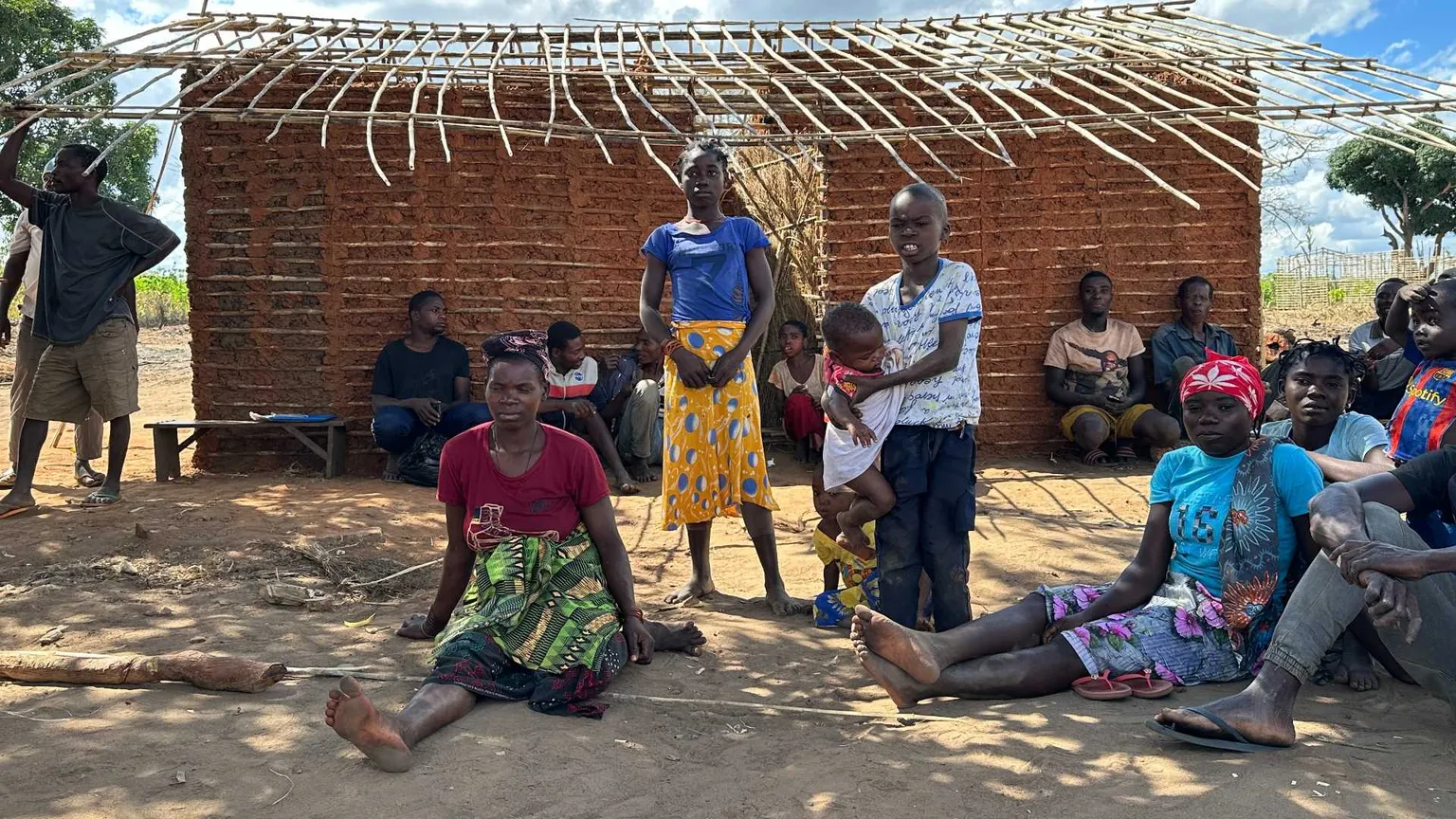 Donne e uomini seduti davanti a una capanna tradizionale di canne nel villaggio di Nannona, nella provincia mozambicana di Cabo Delgado