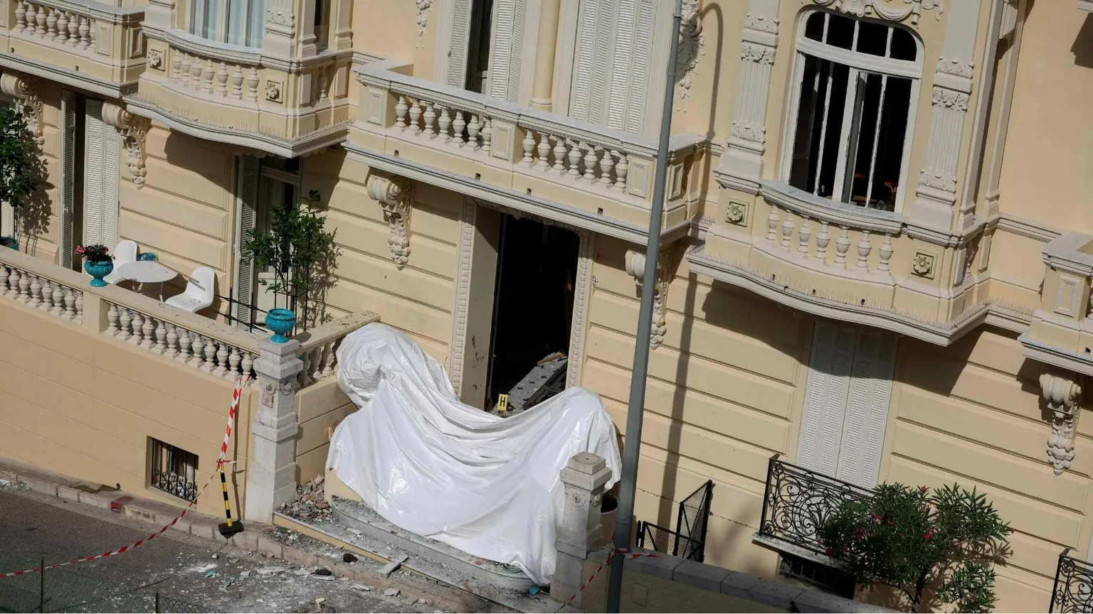 L'ingresso di un edificio è coperto al piano terra da un telo bianco. Al primo piano, un terrazzo.