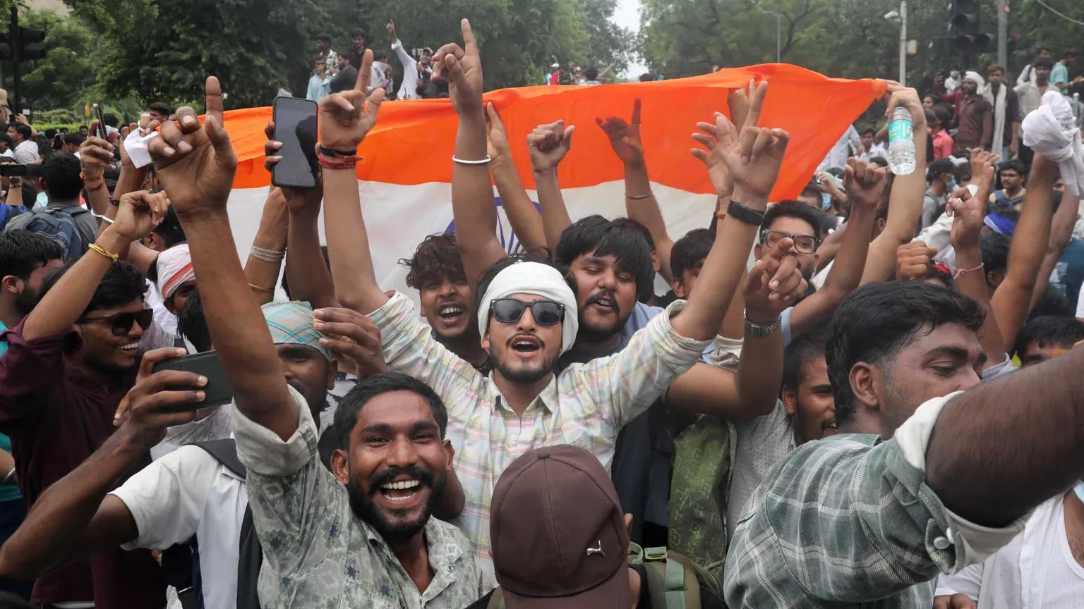 Giovani indiani con le braccia al cielo e il sorriso, davanti a una bandiera dell'India