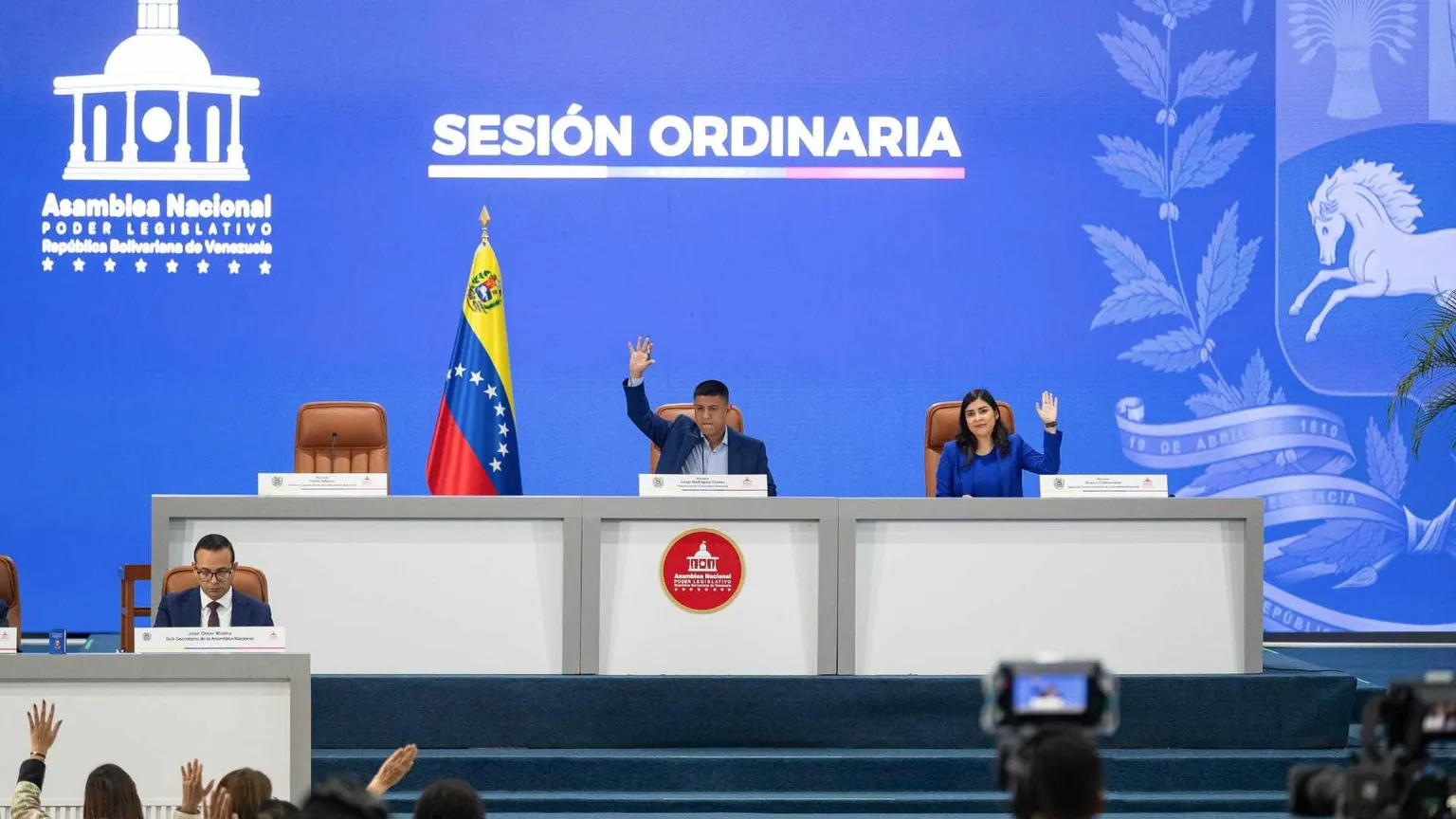 Un lungo tavolo bianco con la bandiera venezuelana e due persone sedute