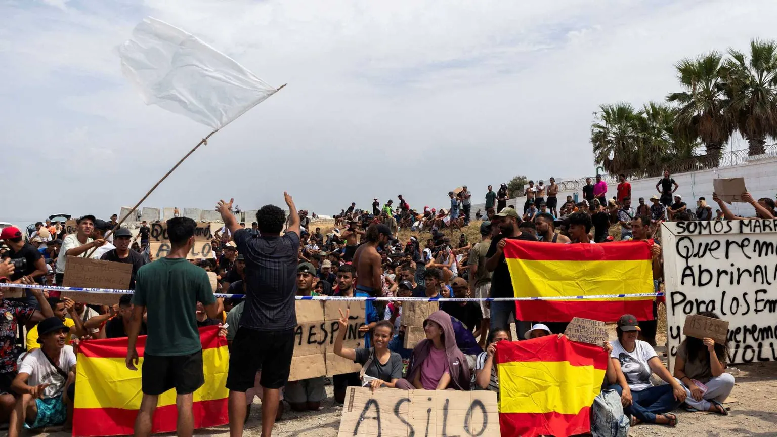 Migranti sventolano bandiere spagnole e cartelli con la scritta "Asilo" nell'exclave di Ceuta