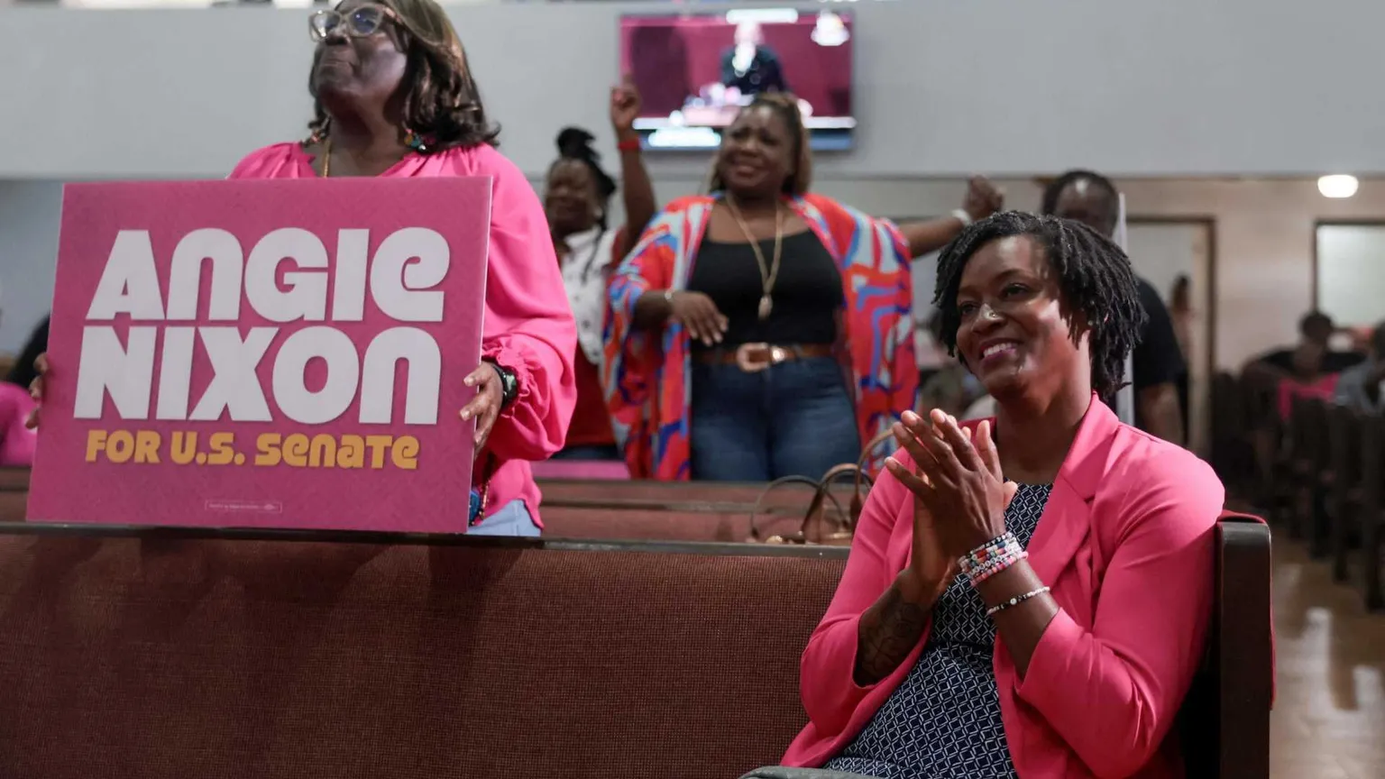 Una giovane donna di colore sorridente, seduta, con una giacca color fucsia