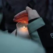 Una candela tra le mani di una ragazza nel luogo del “memoriale” improvvisato a Crans-Montana davanti al locale della tragedia