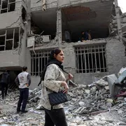 Una donna davanti a un edificio distrutto a Teheran