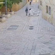 Una vasta via piastrellata, con pochissime persone: un uomo aggredisce alle spalle una suora in abito bianco e velo nero