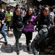 Una ragazza con un giubbino catarifrangente rosa, indossato dagli attivisti di "Standing Together", portata via da due poliziotte in mezzo a una manifestazione