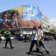Persone camminano per le strade di Teheran. Sullo sfondo, gli ayatollah Khomeini e Khamenei