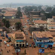 Una strada in terra battuta attraversa la capitale della Repubblica Centrafricana, Bangui. Gli edifici appaiono come fatiscenti. Il colore dominante è l'arancione.