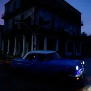 Un'auto anni Cinquanta davanti a una palazzina buia al tramonto all'Avana
