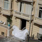 L'ingresso di un edificio è coperto al piano terra da un telo bianco. Al primo piano, un terrazzo.