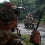 Quattro militari su un mezzo. In primo piano, sfocato, un militare di spalle che parla a un radio trasmettitore