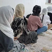 Donne con il velo sedute l'una davanti all'altra, in fila, di spalle
