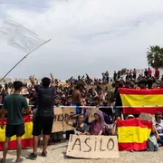 Migranti sventolano bandiere spagnole e cartelli con la scritta "Asilo" nell'exclave di Ceuta