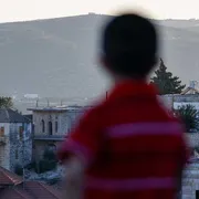 Un bambino palestinese tra le case della cittadina cristiana di Taybeh, a nord-est di Ramallah, in Cisgiordania occupata da Israele. Sullo sfondo, un nuovo avamposto di un insediamento israeliano / AFP