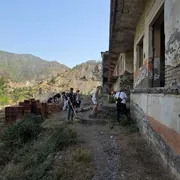 Dei ragazzi muniti di rastrelli e falcette strappano le erbacce di fronte a una prigione abbandonata. Davanti all'edificio giacciono dei mattoni nuovi inutilizzati. Sullo sfondo si vedono le montagne