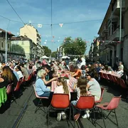 Centinaia di persone siedono attorno a dei tavoli disposti sulla strada