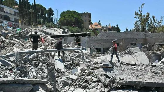 Tre persone camminano tra le macerie di un edificio bombardato. Sullo sfondo, il cielo azzurro
