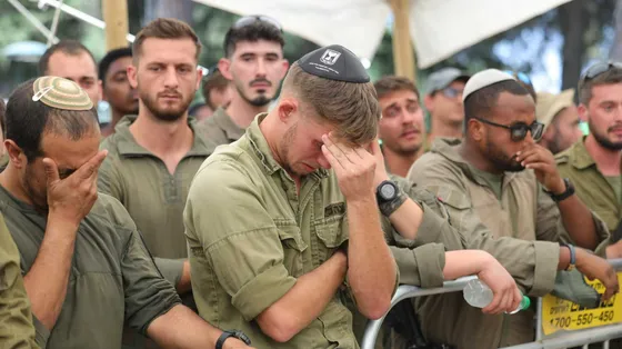 Diversi uomini, in fila, vestiti da militari. In primo piano, un ragazzo che piange e si copre il volto con una mano