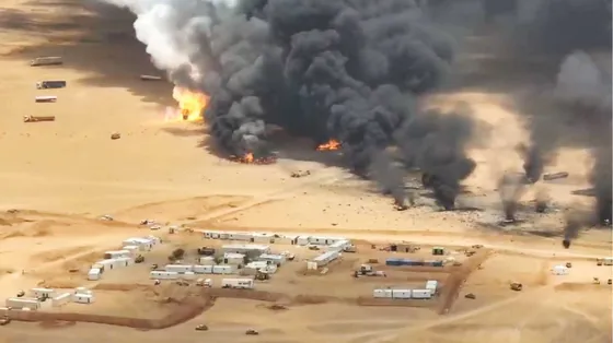 Basse costruzioni bianche in mezzo al deserto di sabbia ocra, sullo sfondo il fumo nerissimo dei bombardamenti