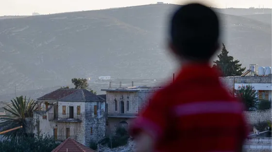 Un bambino palestinese tra le case della cittadina cristiana di Taybeh, a nord-est di Ramallah, in Cisgiordania occupata da Israele. Sullo sfondo, un nuovo avamposto di un insediamento israeliano / AFP