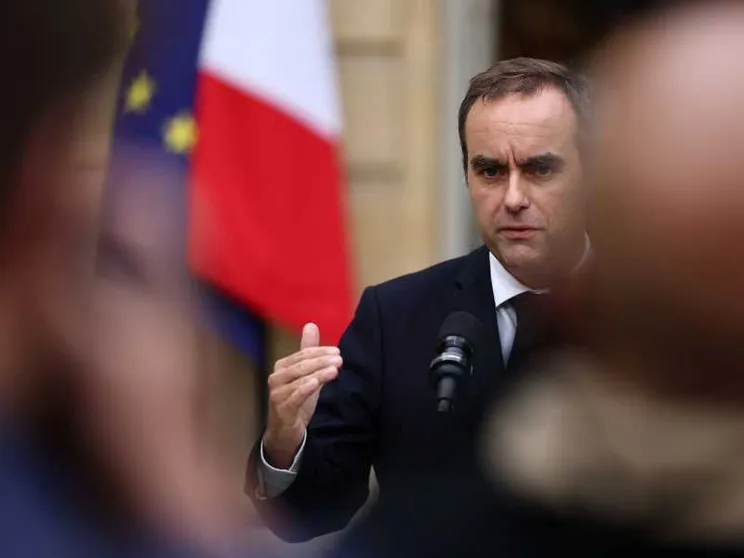 Sebastien Lecornu davanti a un microfono, con un'espressione tesa, la fronte corrugata. Alle sue spalle le bandiere francese e dell'Ue