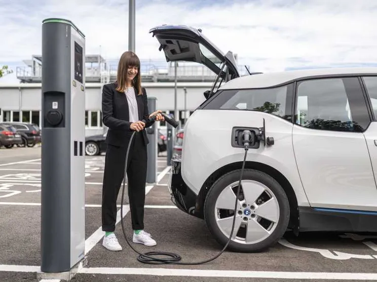 Una ragazza ricarica la propria auto elettrica da una colonnina pubblica