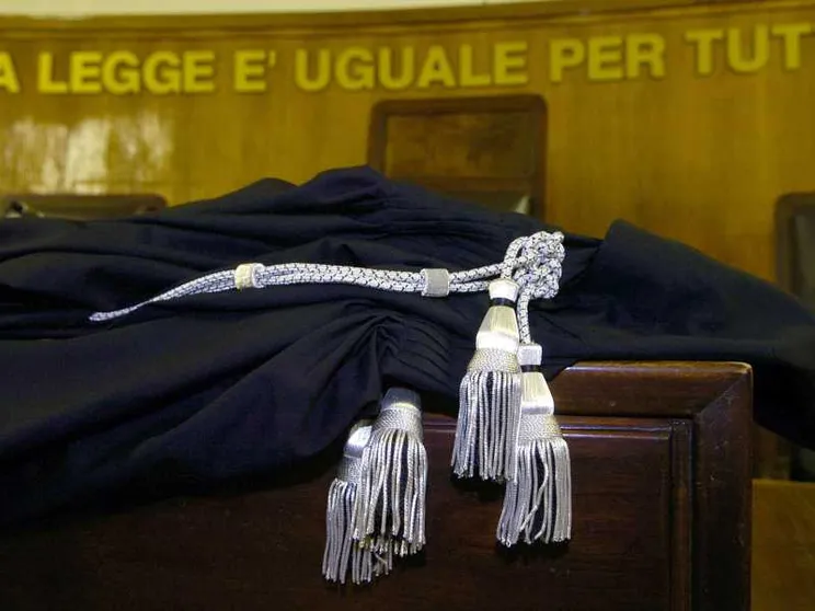 L'immagine ritrae una toga da magistrato sul banco di un Tribunale italiano, sullo sfondo la scritta "La legge è uguale per tutti"