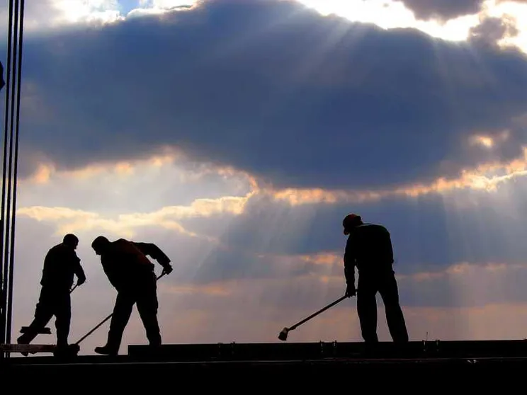 L'immagine mostra tre uomini che stanno lavorando su un ponteggio alla luce di un tramonto