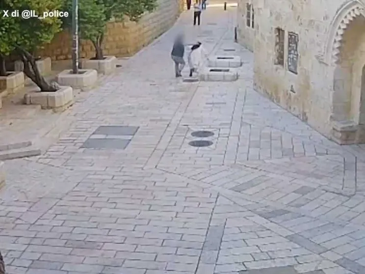 Una vasta via piastrellata, con pochissime persone: un uomo aggredisce alle spalle una suora in abito bianco e velo nero