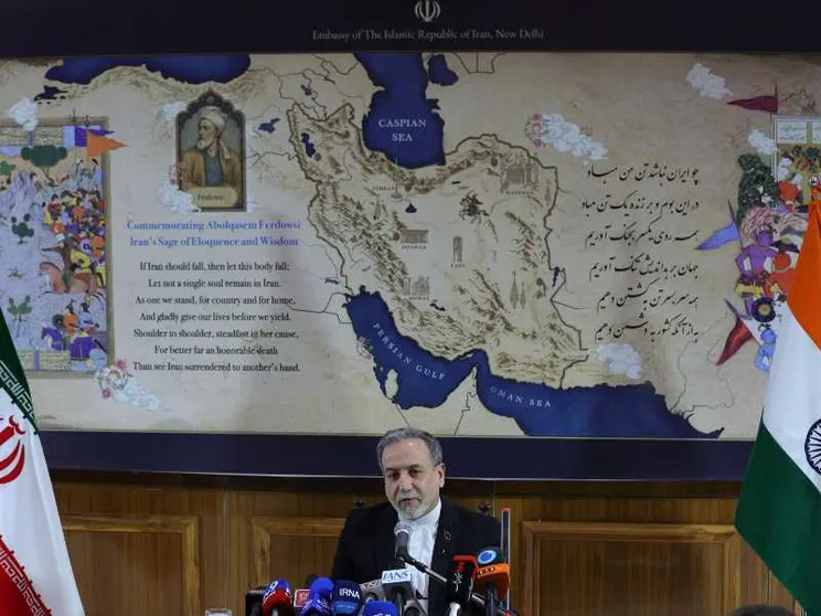 Un uomo in giacca nera e camicia biancia, capelli e barba brizzolati, seduto davanti a una selva di microfoni: alle sue spalle una mappa del Medio Oriente e, ai lati, le bandiere iraniana e indiana