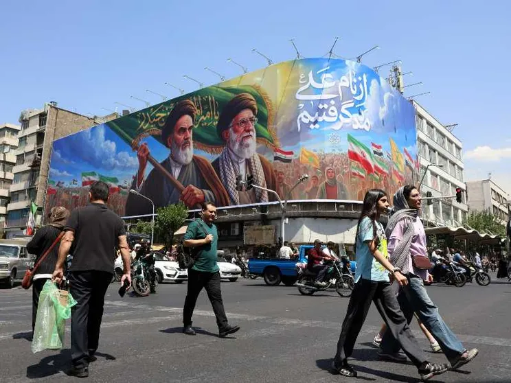 Persone camminano per le strade di Teheran. Sullo sfondo, gli ayatollah Khomeini e Khamenei