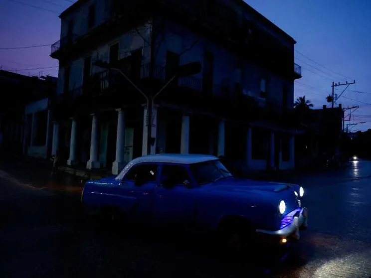Un'auto anni Cinquanta davanti a una palazzina buia al tramonto all'Avana