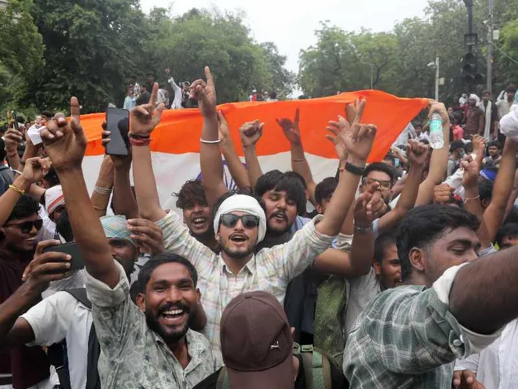 Giovani indiani con le braccia al cielo e il sorriso, davanti a una bandiera dell'India