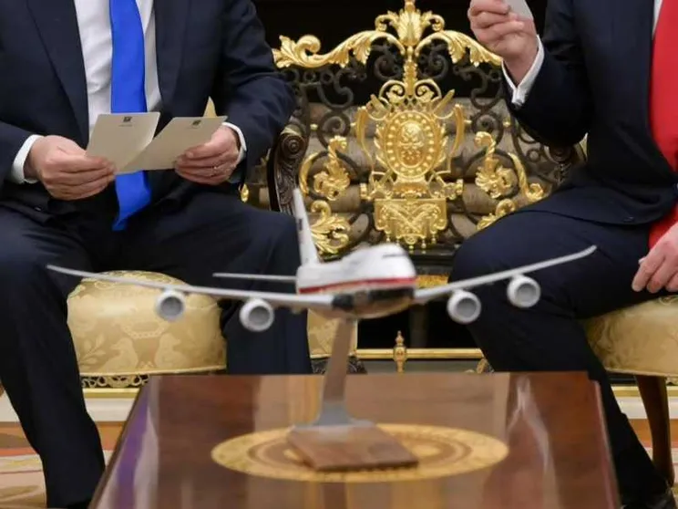Un modellino di un aereo in primo piano. Sullo sfondo due uomini in abiti eleganti che parlano