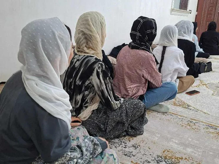Donne con il velo sedute l'una davanti all'altra, in fila, di spalle