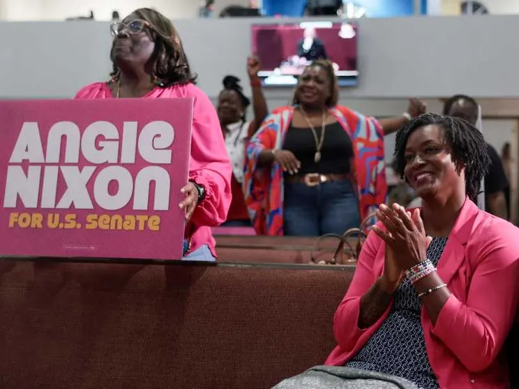 Una giovane donna di colore sorridente,  seduta, con una giacca color fucsia