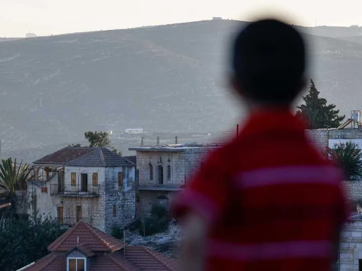 Un bambino palestinese tra le case della cittadina cristiana di Taybeh, a nord-est di Ramallah, in Cisgiordania occupata da Israele. Sullo sfondo, un nuovo avamposto di un insediamento israeliano / AFP