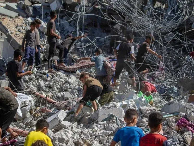 Una decina di persone, tra cui almeno 6 bambini, si muovono sulle macerie di un edificio crollato
