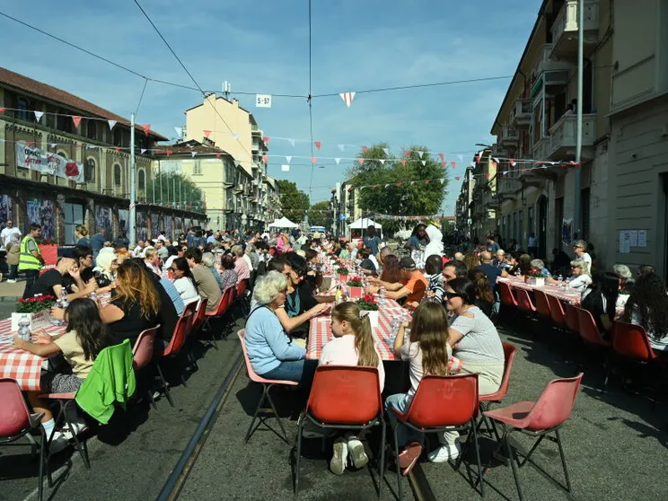 Centinaia di persone siedono attorno a dei tavoli disposti sulla strada