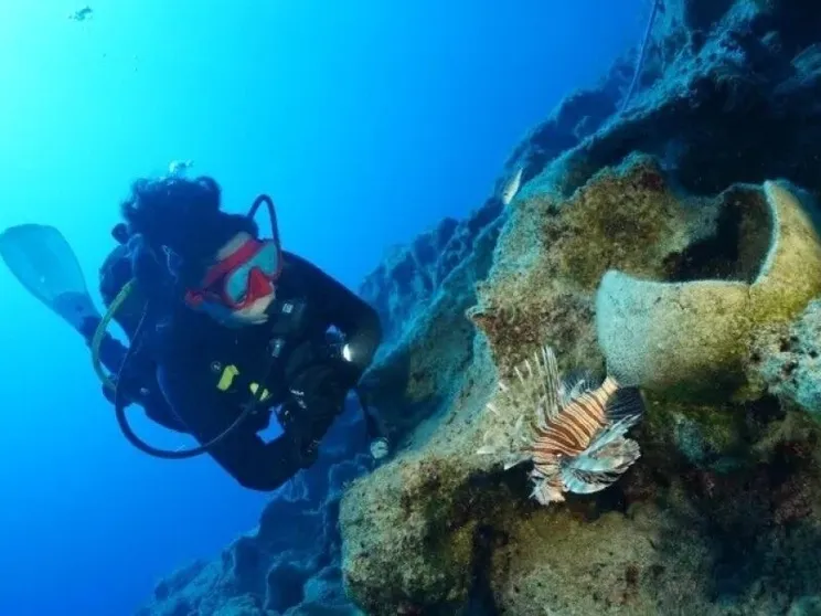 Una donna con muta da sub esplora un fondale marino dove ci sono resti di anfore