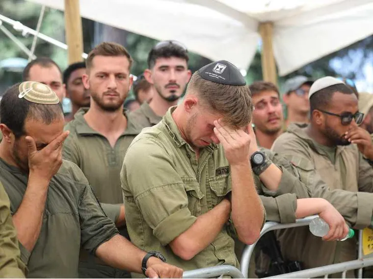 Diversi uomini, in fila, vestiti da militari. In primo piano, un ragazzo che piange e si copre il volto con una mano
