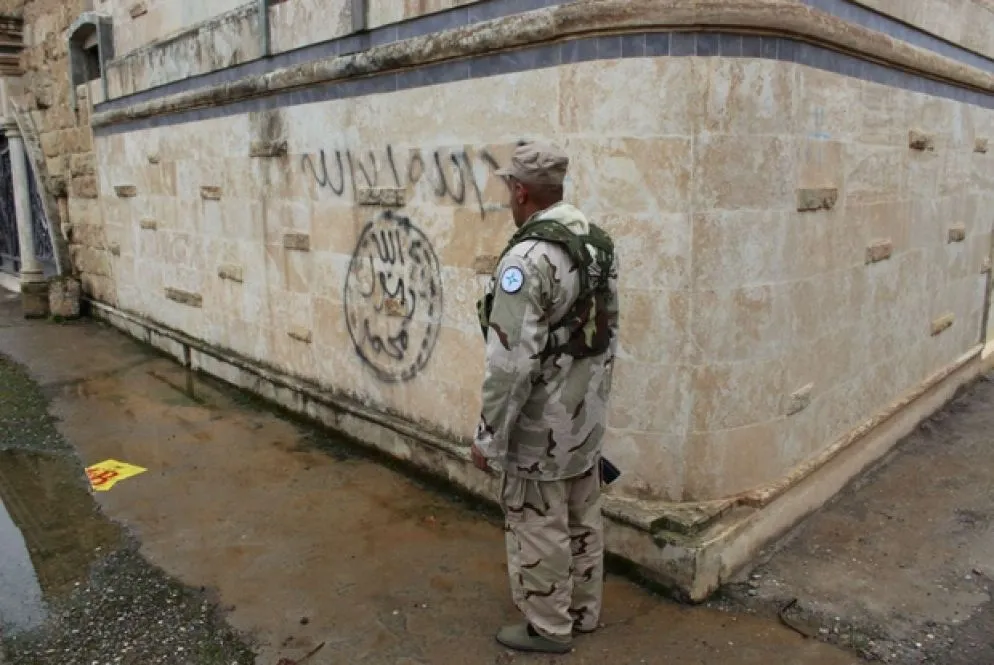 Un poliziotto davanti al simbolo del Daesh su un muro di Karamles